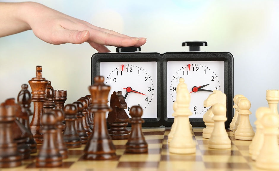 Un arbitre d’échecs en tournoi, debout derrière plusieurs joueurs, avec une pendule d’échecs et des échiquiers en arrière-plan.